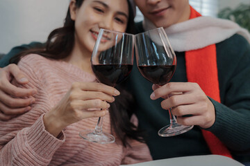 Happy couple wearing Santa hats enjoying wine together on the sofa beside a decorated Christmas tree, celebrating the festive holiday season at home.