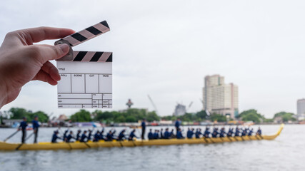 Clapperboard in hand with traditional longboat rowing team in the background. Perfect concept for filmmaking, behind the scenes, teamwork, and documentary storytelling.