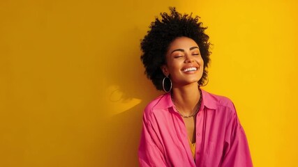 Smiling woman with curly hair wearing a pink shirt and hoop earrings against a bright yellow background.