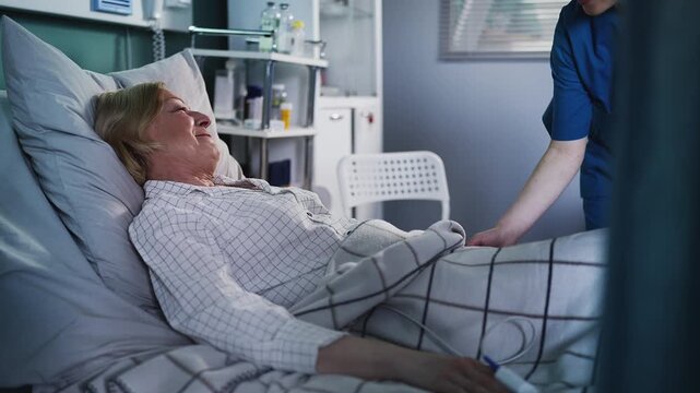 Nurse assisting thankful senior ICU patient, adjusting blanket for her comfort