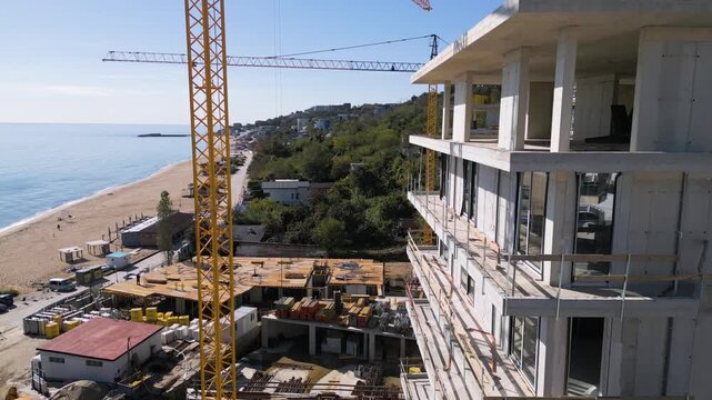 Aerial view of a construction site with tower cranes building modern apartments near the sea coast on a sunny day. Urban development concept