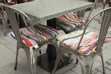 Metal chairs with colorful cushions and a table with a stone top, a café, a sidewalk.