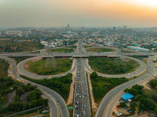 Aerial view of the Golf Course Extension Road interchange, a symphony of concrete and green against the hazy horizon, Gurugram, Haryana, India.