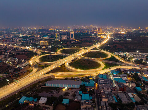 Aerial view of a mesmerizing highway cloverleaf interchange illuminated by golden streetlights under a twilight sky, Golf Course Extension Road, Gurugram, Haryana, India.