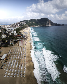 Aerial view of the sun-kissed Cleopatra Beach where azure waves meet the golden sands and the iconic Alanya Castle stands guard, Alanya, Antalya, Turkey.