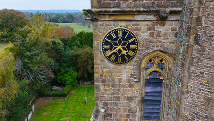 Aerial view of the clock tower of St Mary's Church showing Roman numerals, standing tall against a backdrop of green trees, Leigh, England, United Kingdom.