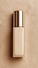 A beige foundation bottle with a gold cap placed on a textured brown surface. The bottle is sleek and modern, suitable for cosmetic use.