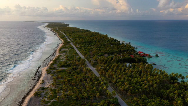 Aerial view of a narrow strip of land with lush green vegetation, bordered by a road and azure waters, Rangiroa, Tuamotu Islands, French Polynesia.
