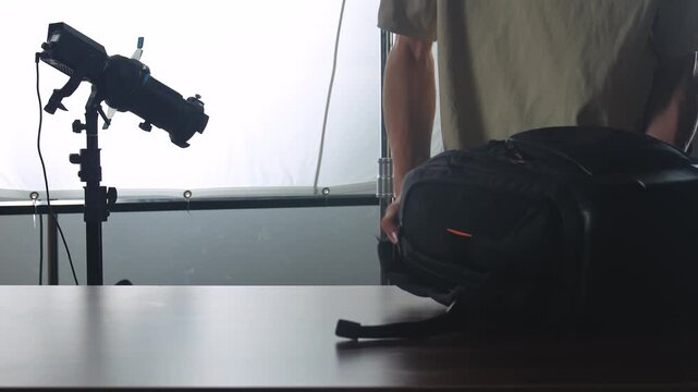 A man organizing camera gear on a table with studio lighting, showcasing lenses and a camera bag.