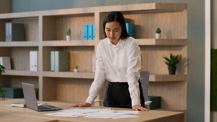 Asian Chinese business woman female secretary manager employer Korean Japanese businesswoman worker looking documents reviewing report paperwork checking data project using laptop device indoor office