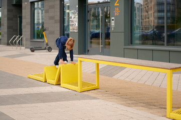 child playing on modern yellow playground feature outside urban building, exploring creativity and balance. scooter and residential background emphasize urban park setting © khmelev