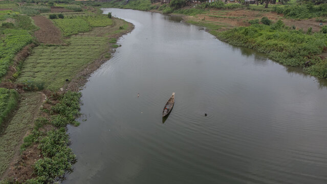 Aerial view of a canoe glides serenely on the river, reflecting the sky above, framed by verdant riverbanks, Makurdi, Benue, Nigeria.