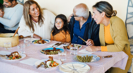 Happy latin mother, daughter, grandfather, grandmother and father having fun eating together at home - Hispanic cultures and family lifestyle concept - Main focus on kid face