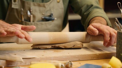 Close up talented unknown unrecognizable Caucasian man male hands arms guy small business owner potter craftsman businessman knead clay dirt mud using rolling pin equipment crockery tool indoor studio