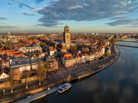 Aerial view of the Lebuinus Church towering over the terracotta rooftops, golden light bathing the IJssel river, Deventer, Overijssel, Netherlands.