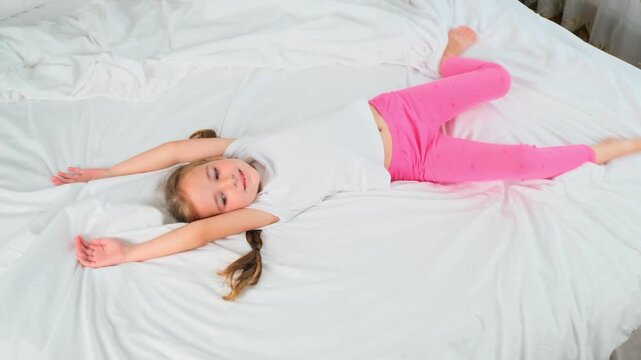 Top view of cute little girl lying and smiling on bed at home