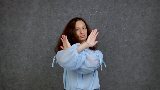 Beautiful girl with curly long hair in a blue blouse 18-25 years old shows with her hands the word no and shakes her head to the right and left