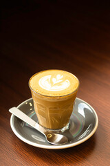 Warm coffee drink with latte art served in glass on a dark wooden table