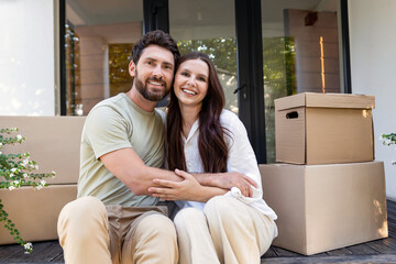 Obraz premium Happy couple sitting at the entrance of their new accommodation and looking contented