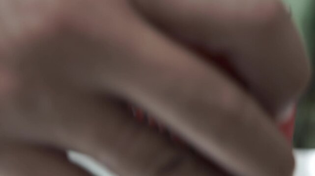Close-up of a hand opening the pull tab of a cold red soda can with water drops