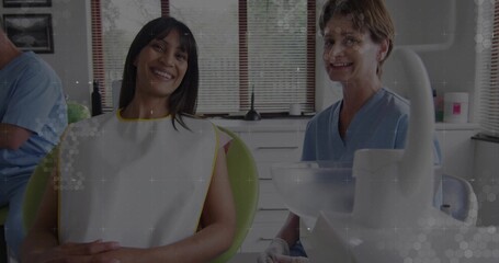 Smiling patient wearing protective bib sitting in dental chair in clinic, with dentist in scrubs