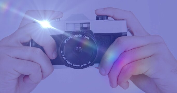 Fototapeta Holding vintage rangefinder camera to eye on purple backdrop, firing flash producing rainbow flares