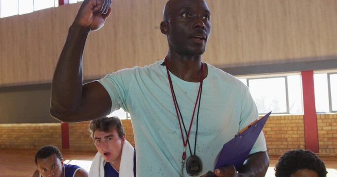 Fototapeta Motivating coach raising fist, instructing basketball players in gym with stopwatch and clipboard