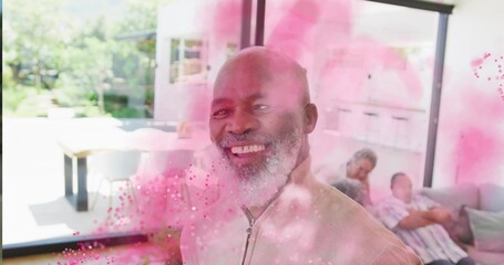 Smiling African American man standing at sliding glass door, with pink powder swirling