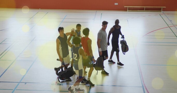 High-fiving six male basketball players leaving gym court, with duffle bags, jerseys, sneakers