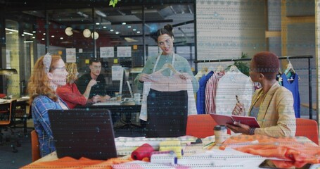Presenting model holding pastel blouse at studio table, with clothing rack and fabric swatches