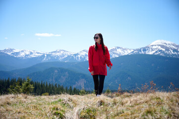 Naklejka premium Hiker girl on background of snowy mountains. Young female in red sport jacket and sunglasses hiking in the mountains. Incredible landscape reflects peace and freedom.