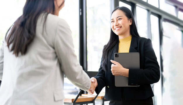 Two Asian businesswomen finalize a deal with a firm handshake in the office.