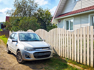Sedan parked beside a wooden fence near a house on a sunny day in a quiet neighborhood