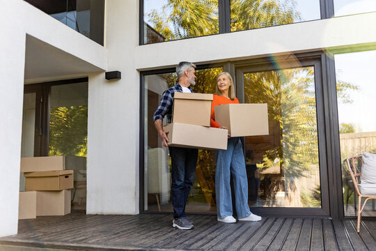 Senior man and woman transporting packed cardboard boxes into new house - Powered by Adobe