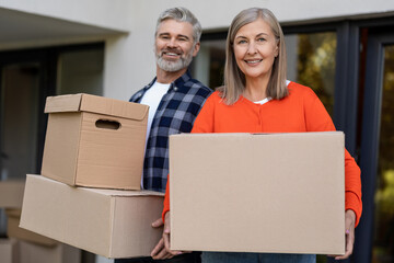 Happy senior couple moving boxes outside residential entrance
