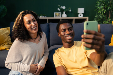 Happy diverse couple taking selfie with smartphone at home