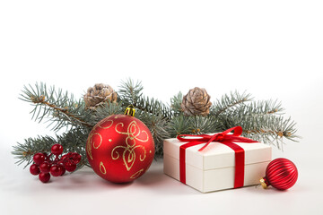 Gift in a white box with a red ribbon, fir branches and Christmas decorations on a white background
