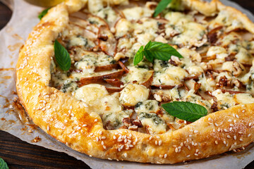 Baked galette or open pie with pear, blue cheese and nuts on the wooden table.