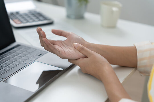 Asian young woman working in office with a carpal tunnel syndrome or wrist joint inflammation, hand muscle inflammation from office syndrome , hand muscle pain from working