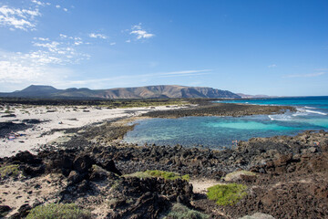 View of the rugged volcanic rocks meet the turquoise waters, under a vast blue sky with scattered clouds, creating a serene yet dramatic seascape, Lanzarote, Canarias, Spain.
