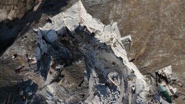 Aerial view of the stark white quarry contrasting against the rugged terrain, with textures highlighting the industrial extraction site, Levigliani, Toscana, Italy.