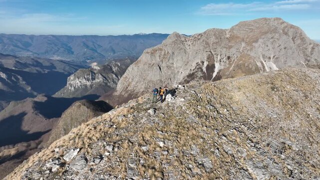 Aerial view of a rugged mountain peak with hikers, showcasing the textures of rock and sparse vegetation, Levigliani, Toscana, Italy.