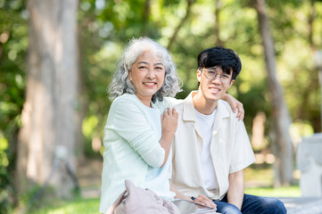 Fototapeta premium Old woman grandmother holding hugging shoulder of young man grandson while sitting on bench in park.