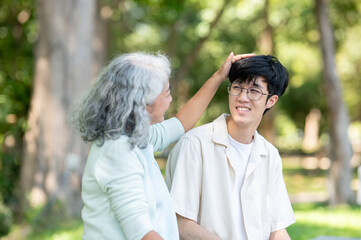 Obraz premium Old woman grandmother patting head of a young man grandson while sitting on bench in garden or park.