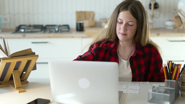Teen girl at laptop desk study with flashcard and pencil organizer in kitchen setting completing homework and online assignment student focus education routine with notebook and book study laptop