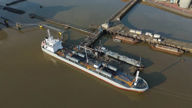 Aerial view of a tanker ship docked near jetties, contrasting with the muddy water and the industrial infrastructure, Purfleet-on-Thames, England, United Kingdom.