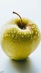 Dew drops adorn a fresh golden apple on a white background