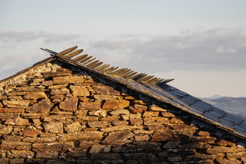 Stone houses in the mountains of A Fonsagrada, Lugo, Galicia, Spain. Traditional Galician mountain village with stone walls wooden details and black slate roofs on a sunny day in northern Spain.
