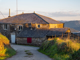 Stone houses in the mountains of A Fonsagrada, Lugo, Galicia, Spain. Traditional Galician mountain village with stone walls wooden details and black slate roofs on a sunny day in northern Spain.