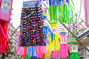 商店街の軒先に飾られた色鮮やかな紙細工やモールでできた七夕飾りが風に揺れる賑やかな夏の風景です